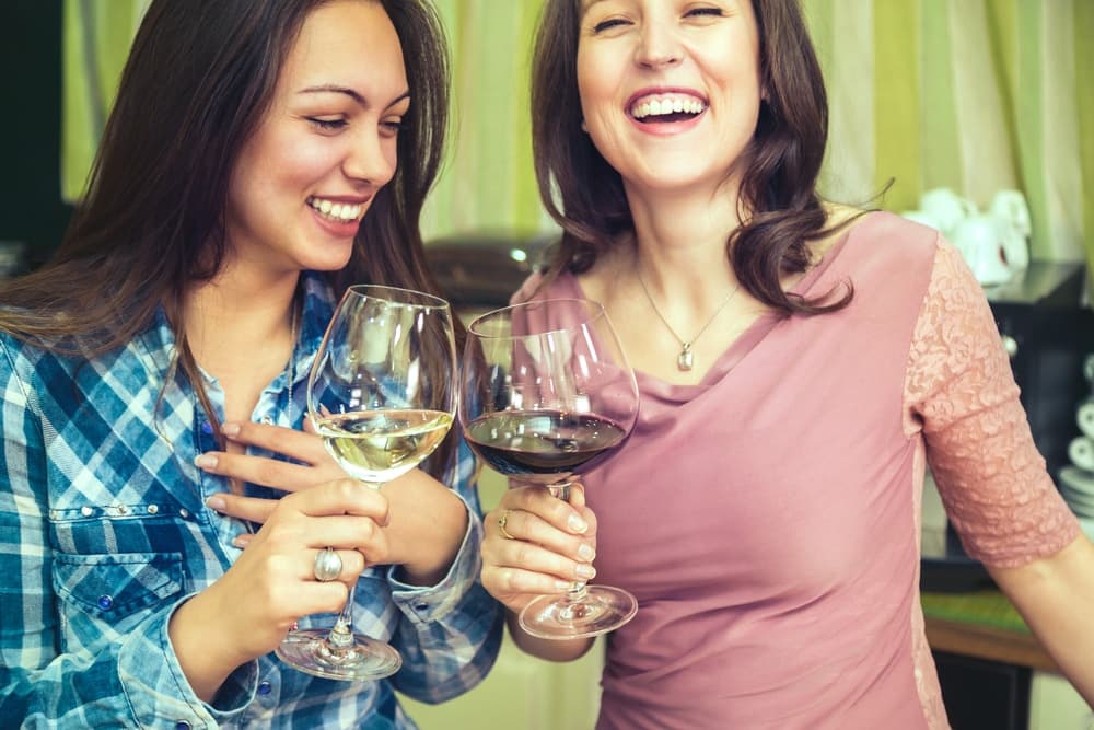 Two women joyfully clink wine glasses while smiling at each other.