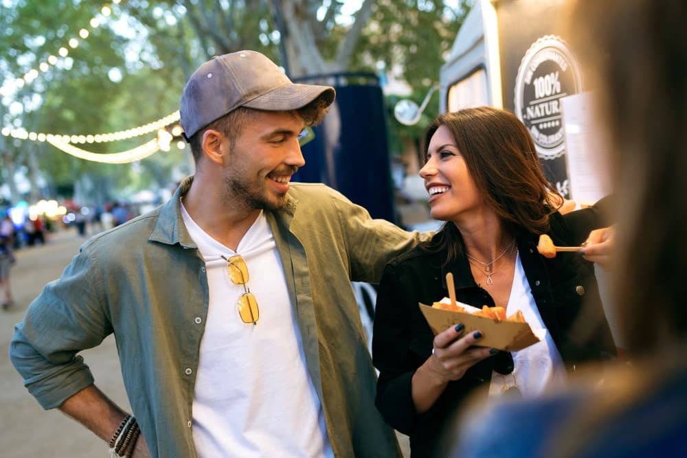 A smiling man and woman enjoy each other's company while sharing food at an outdoor event.