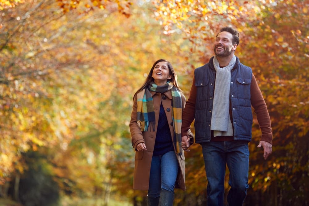 A couple joyfully walks hand in hand through a vibrant autumn landscape.