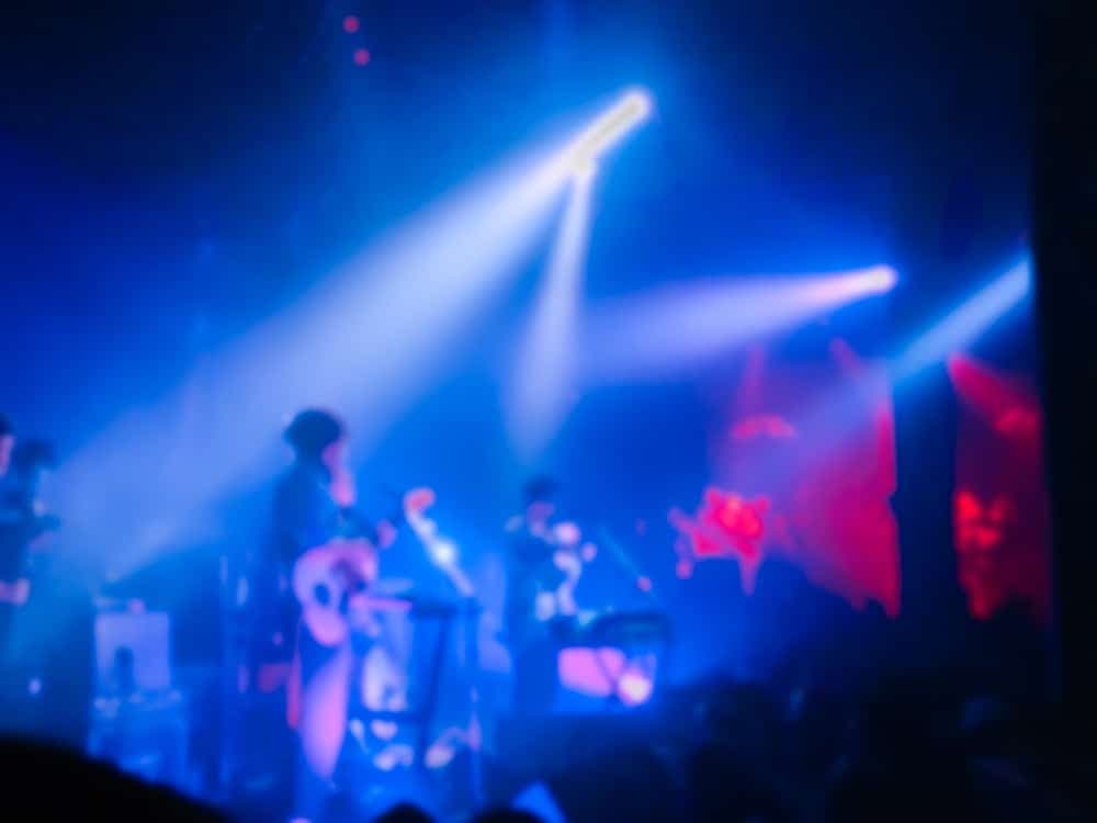 A blurred photo of a live music performance with blue and purple lighting.