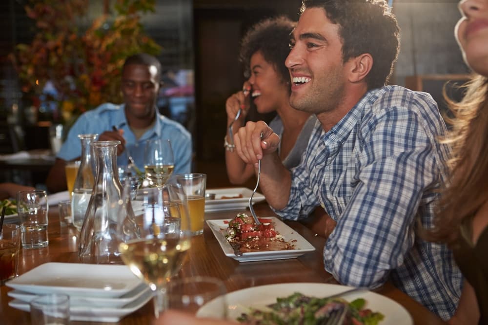 A group of people enjoys a lively dinner conversation at a table filled with food and drinks.