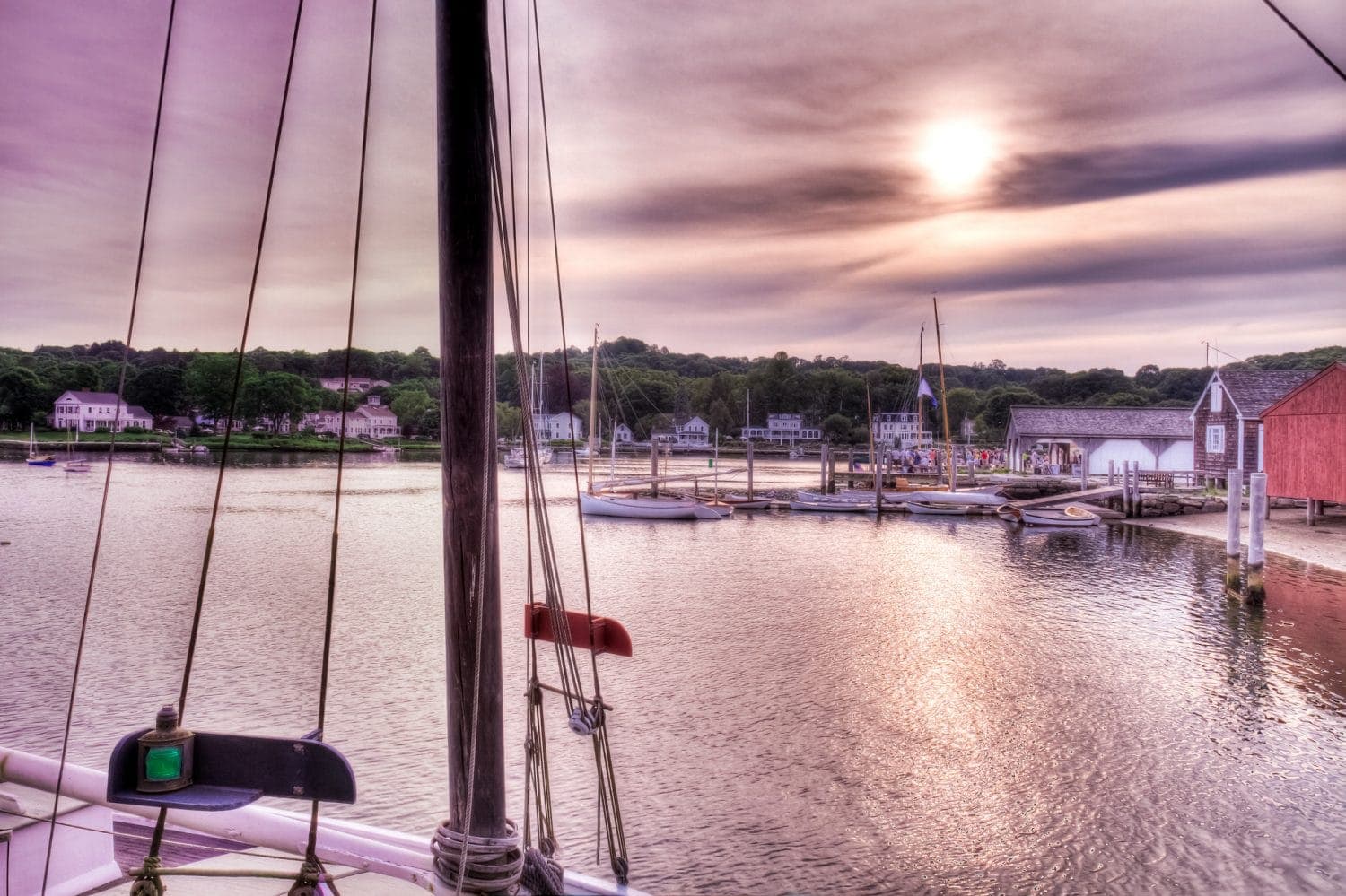 Sunset over a serene harbor with sailboats and docked vessels.