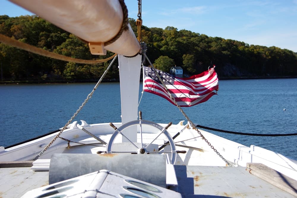 View from the bow of a boat with a waving American flag and a calm water backdrop.