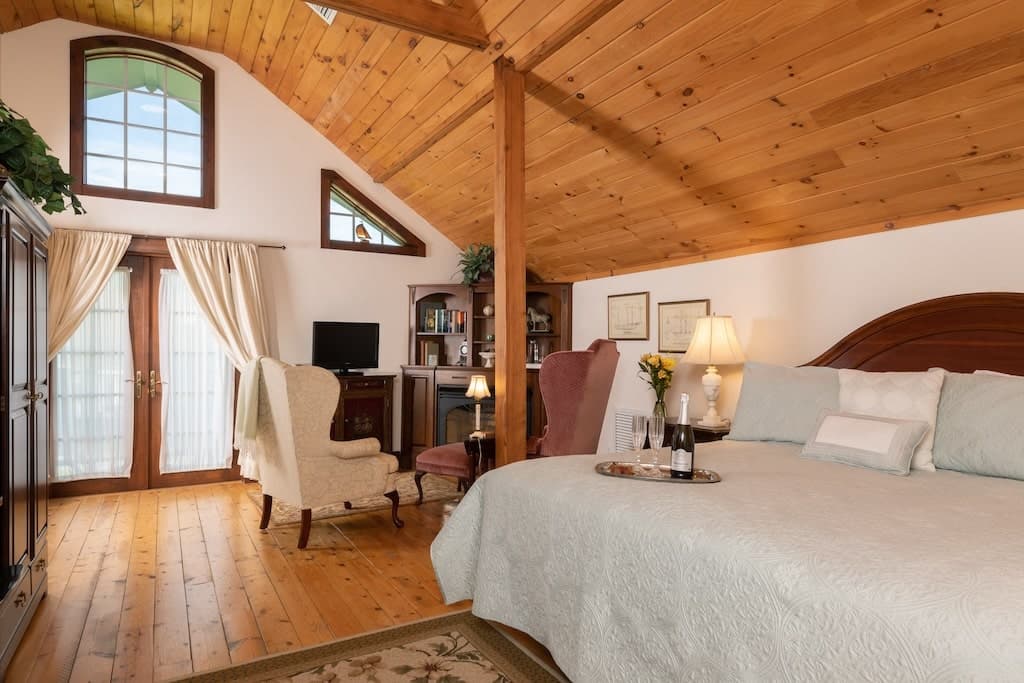 A cozy bedroom with wood paneling, featuring a large bed, a sitting area, and large windows.