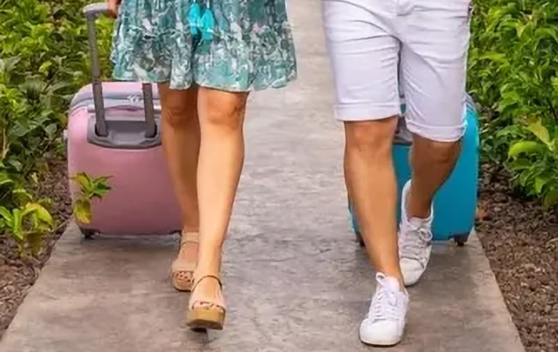 Two people walking on a path with colorful suitcases beside them.