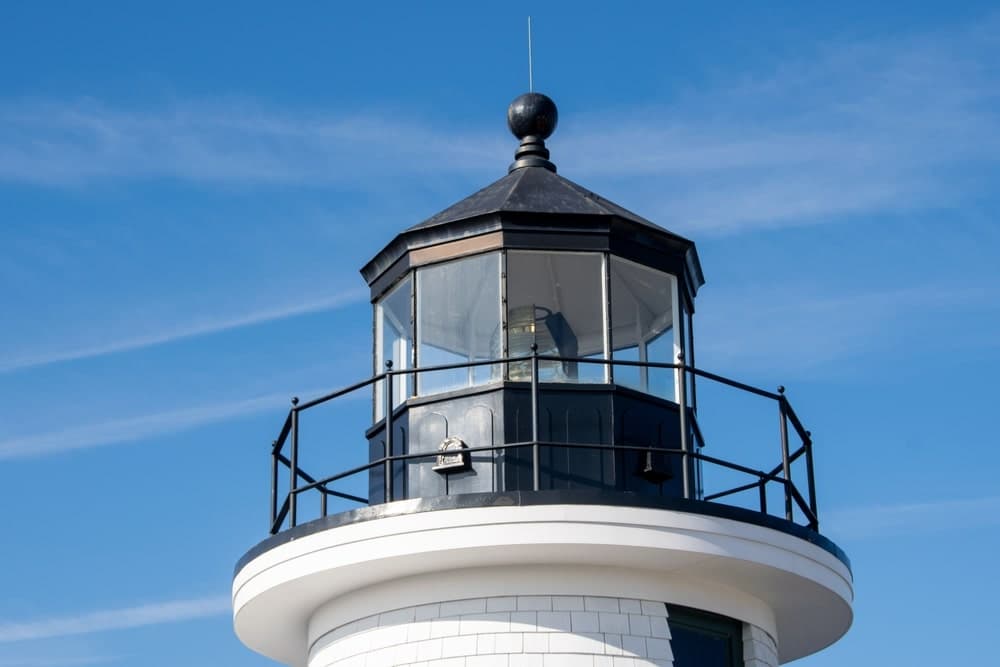 A close-up view of a lighthouse lantern room against a clear blue sky.