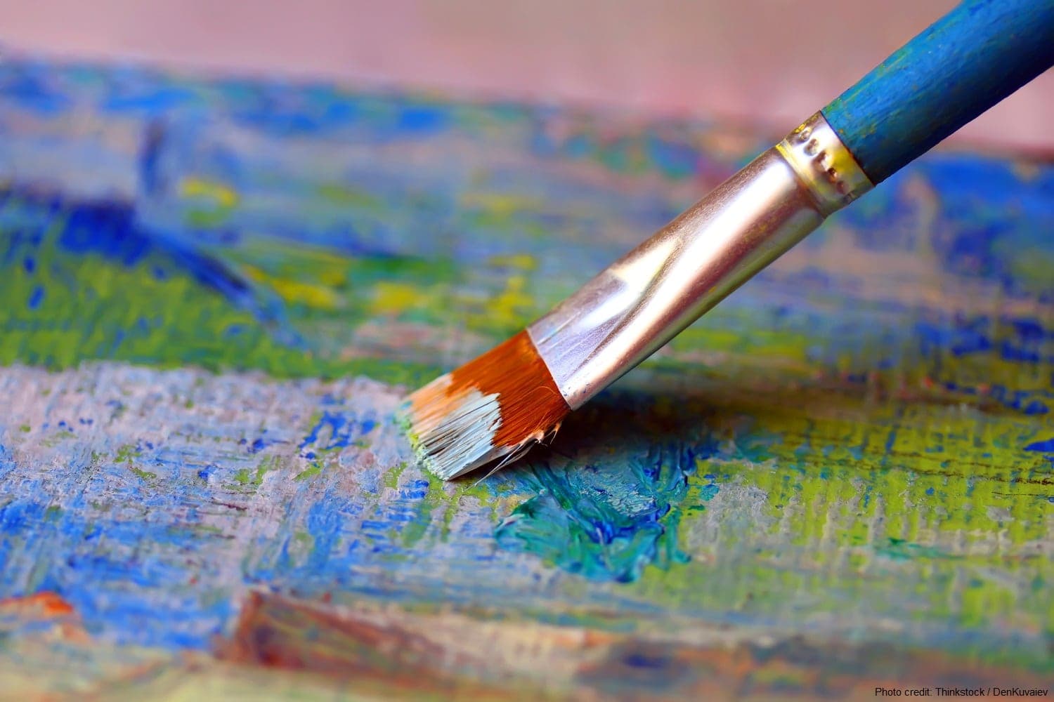 A paintbrush with a blue handle rests on a colorful palette of wet paint.