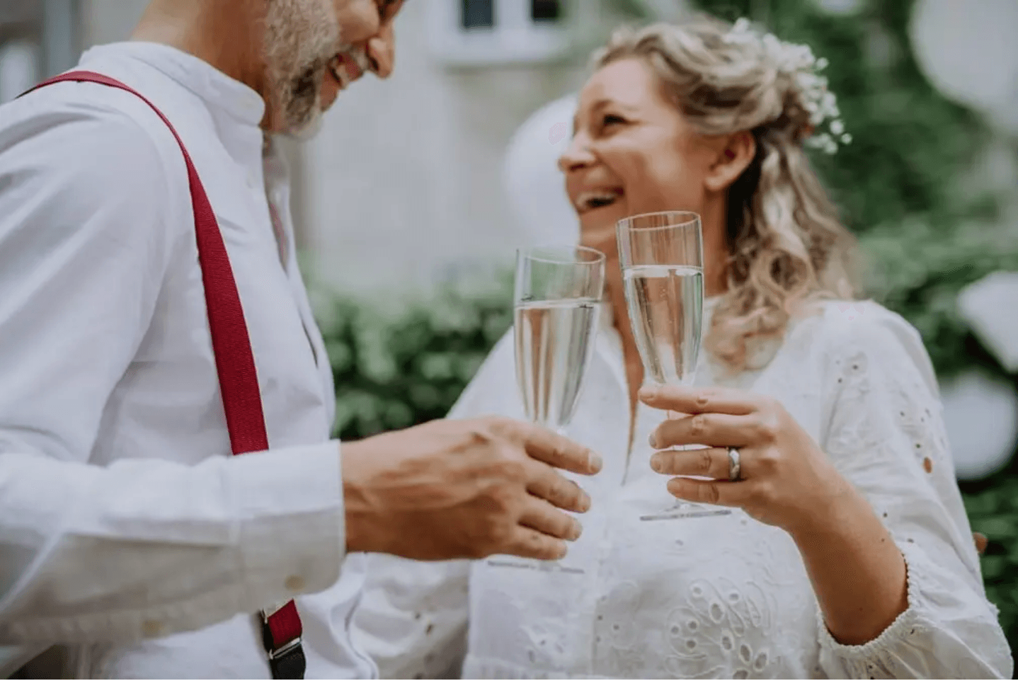 A couple joyfully toasts with champagne glasses in a lush outdoor setting.