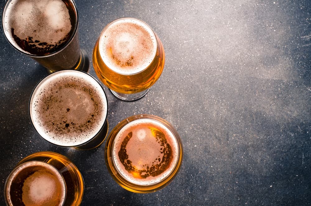 Five glasses of beer in various shades, arranged on a dark surface.