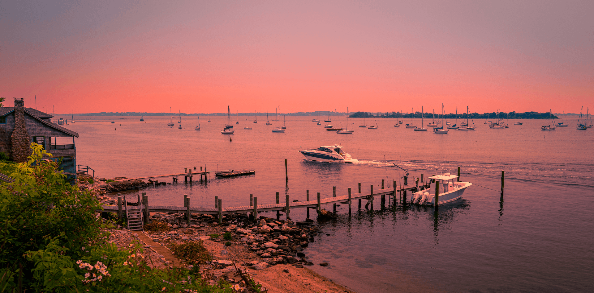 A serene waterfront scene at sunset featuring boats near a marina and a dock.