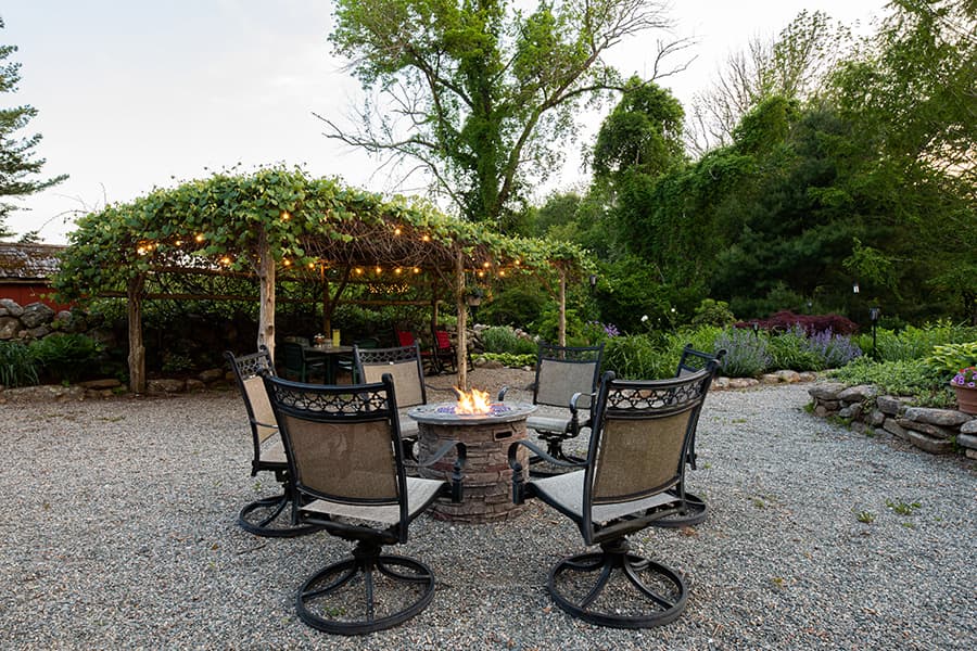 A cozy outdoor seating area with a fire pit surrounded by gravel and lush greenery.