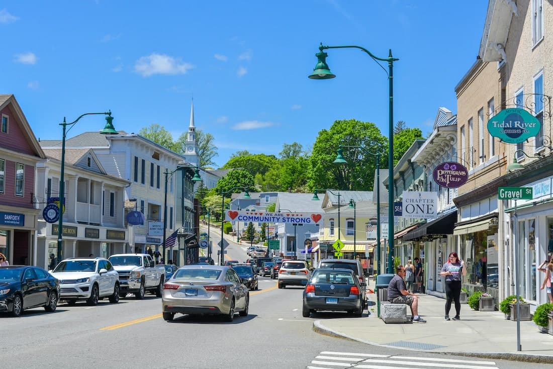 A vibrant small town street bustling with cars and pedestrians, featuring shops and a banner reading "COMMUNITY STRONG."
