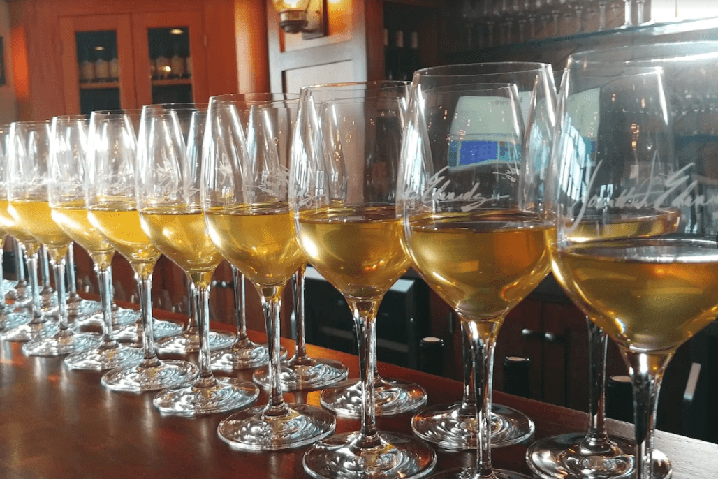 A row of elegant wine glasses filled with golden liquid sits on a bar counter.