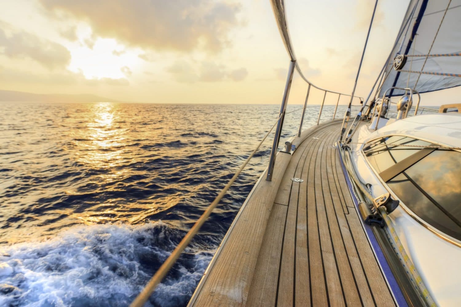 A sailboat glides over calm waters at sunset, with warm hues reflecting on the surface.