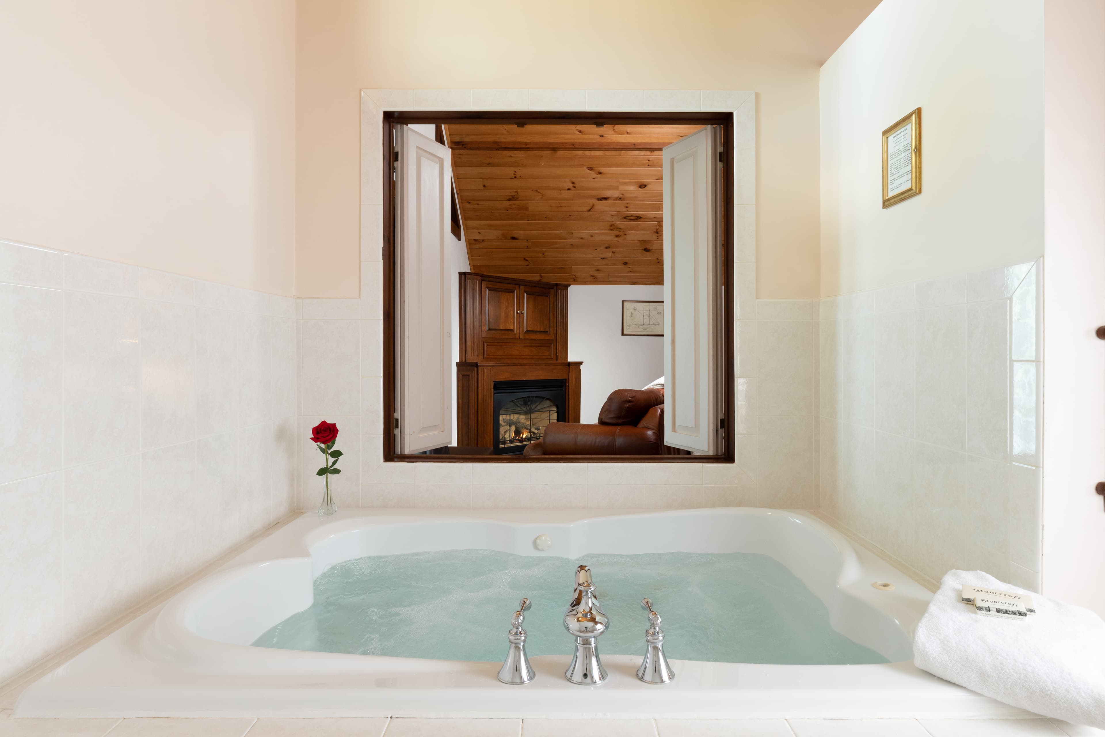 A clean, bright bathroom with a jetted soaking tub, a single red rose, and two flutes of champagne, creating a relaxing, romantic atmosphere.