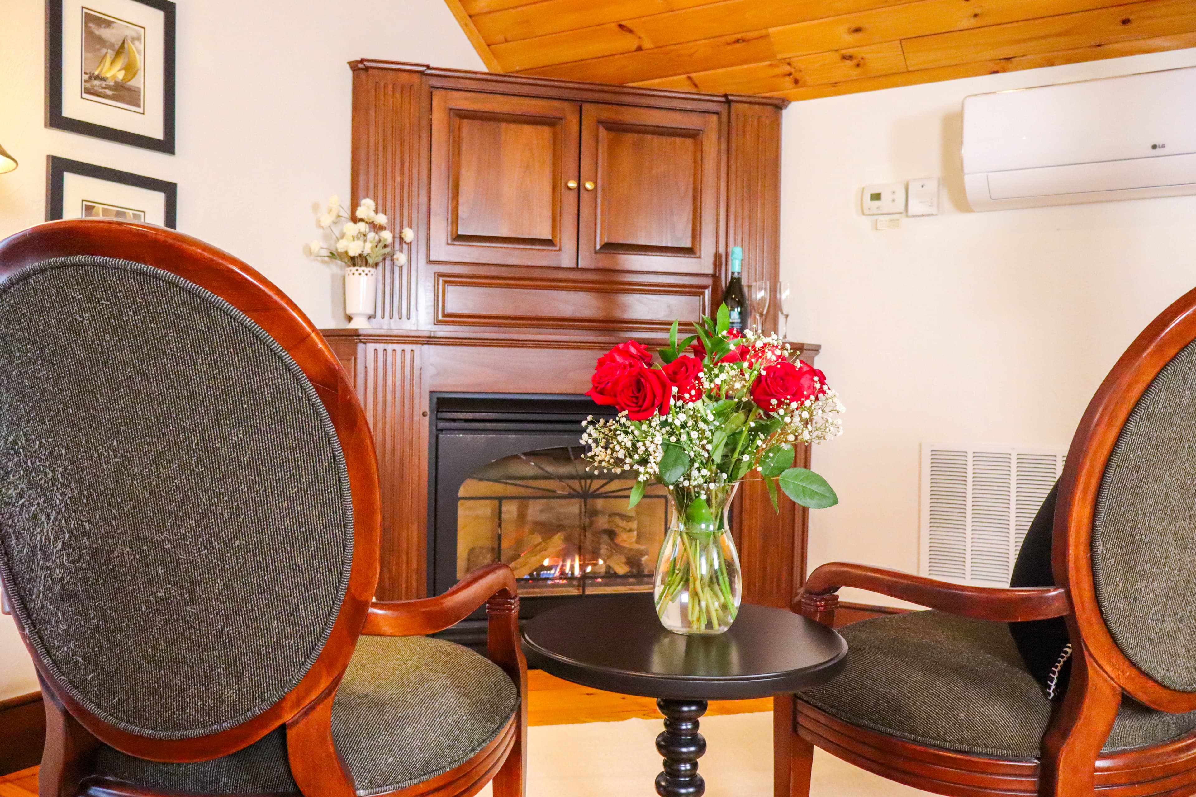 A cozy seating area with two chairs, a small table, and a vase of red roses near a fireplace.