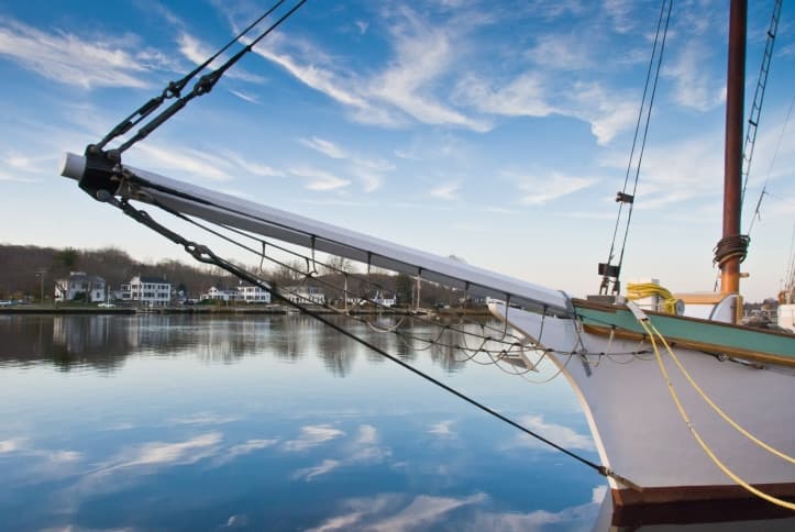 Sailboat docked beside a calm river reflecting the sky.