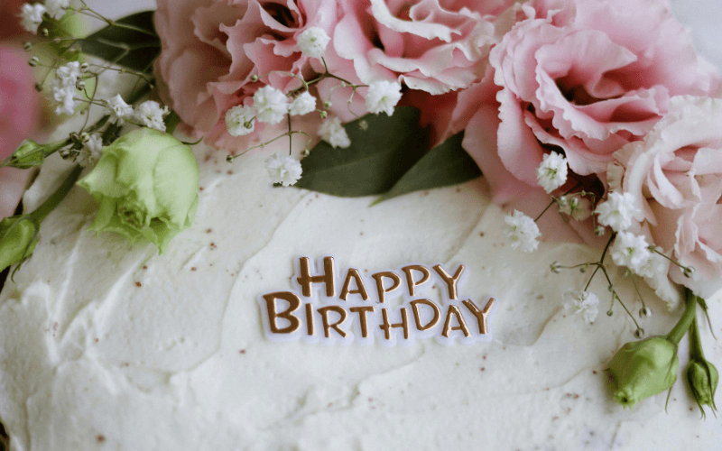 A decorated birthday cake topped with flowers and "Happy Birthday" lettering.