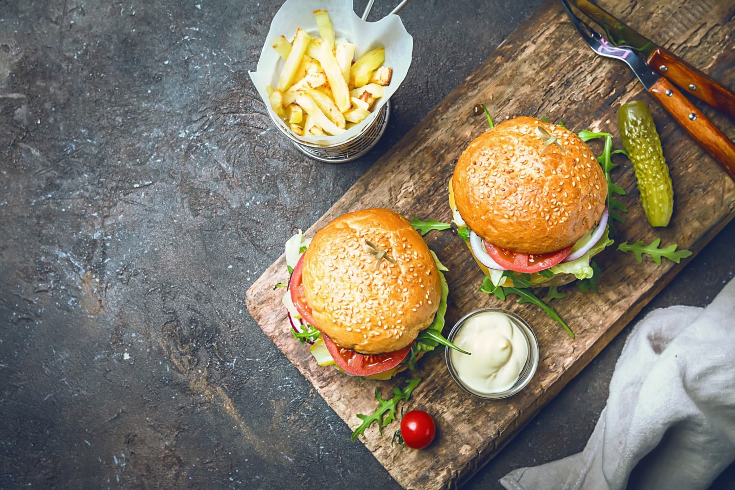 Two sesame-seed burgers with lettuce, tomato, and a side of fries on a wooden board.