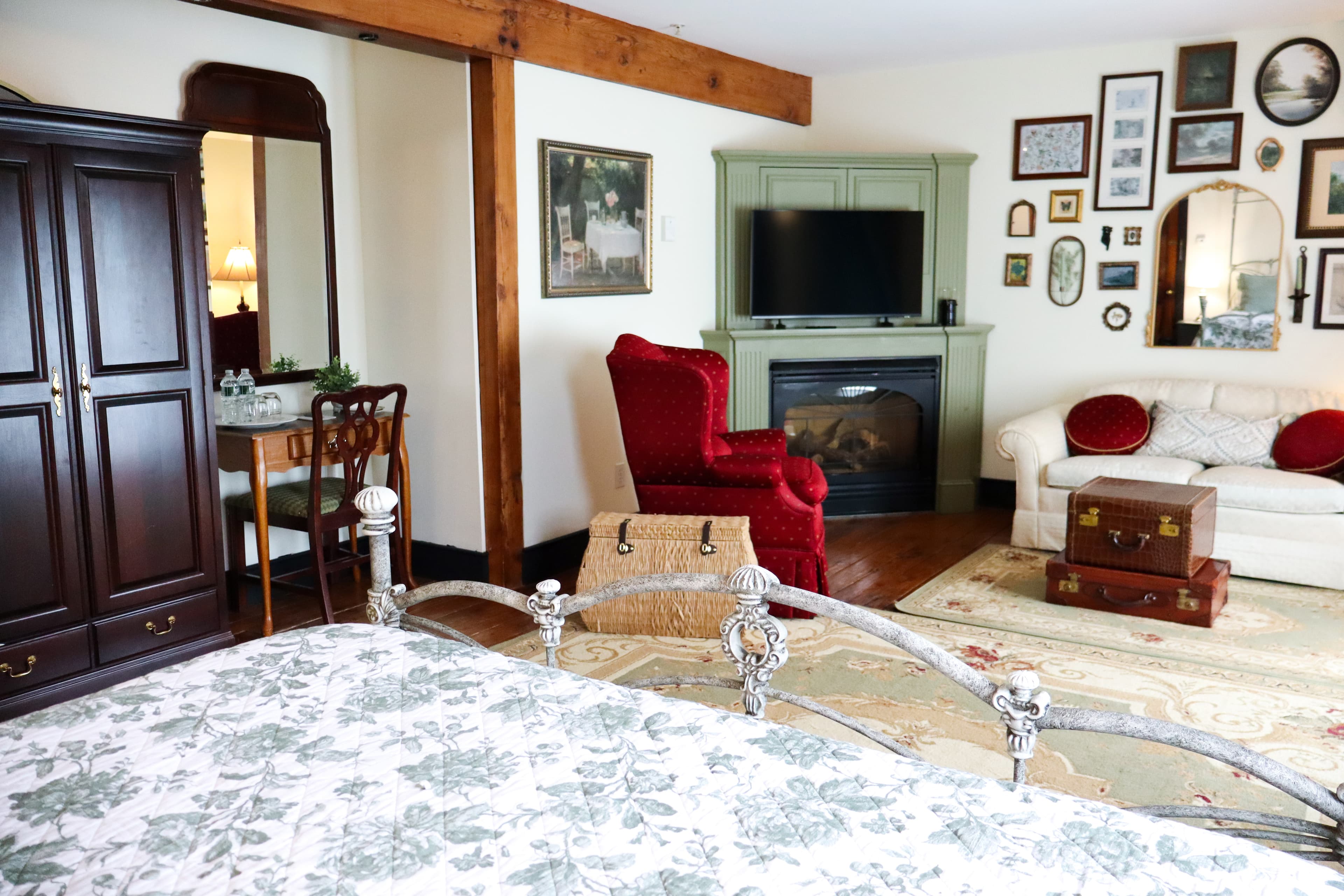 A cozy bedroom featuring a bed with floral bedding, a red armchair, a fireplace, and various wall decor.