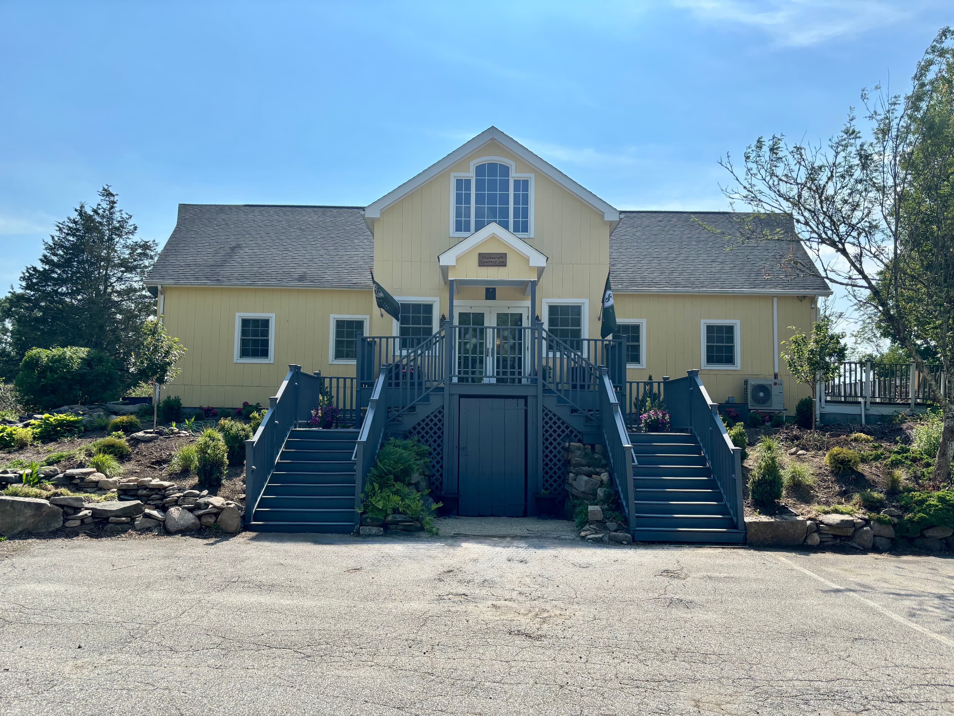 Yellow house with a sloped roof and stairs leading to the entrance, surrounded by landscaped gardens.