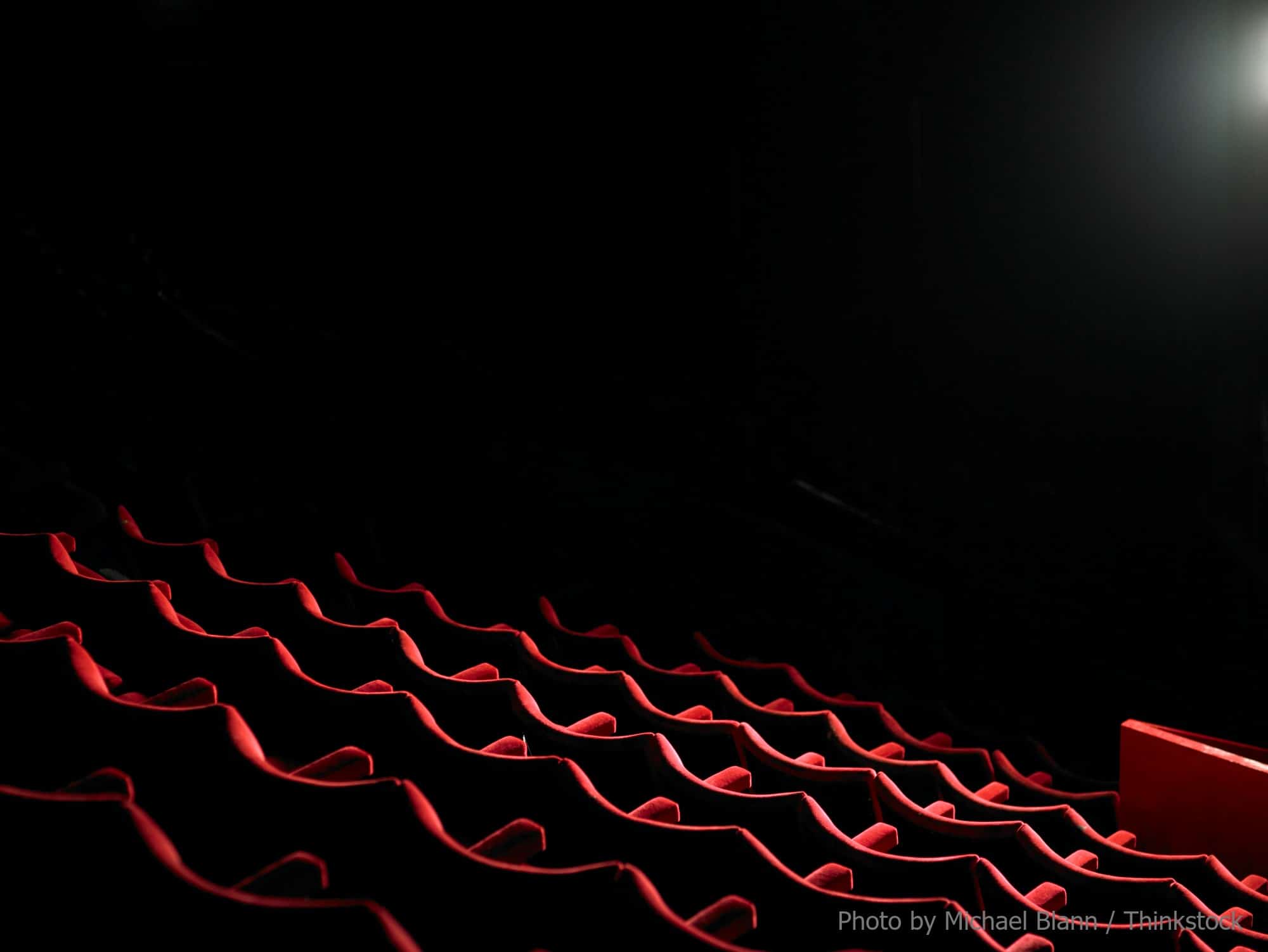 Rows of red theater seats illuminated by a spotlight against a dark background.