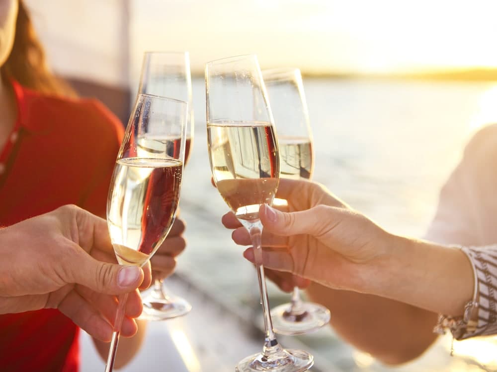Cheers with champagne flutes at sunset by the water.
