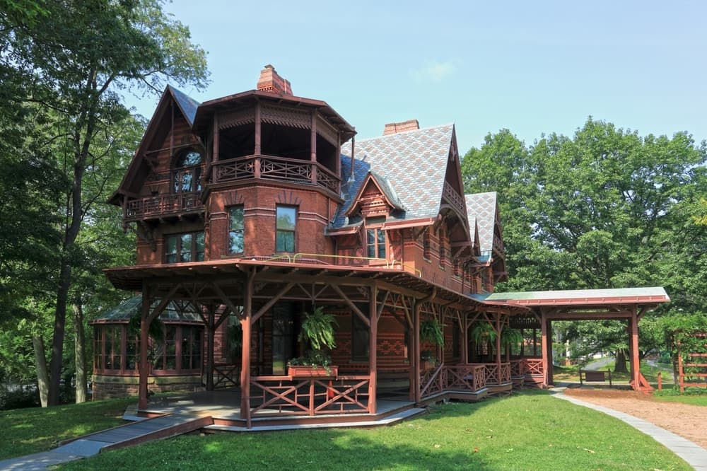 A large, intricately designed Victorian-style wooden house surrounded by greenery.