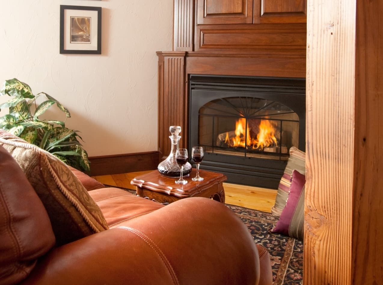 Cozy living room with a fireplace, a leather couch, and wine glasses on a small table.