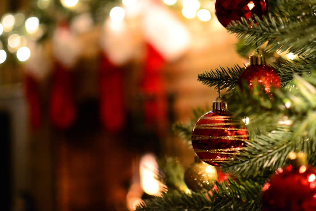 A festive Christmas tree decorated with red and gold ornaments, with stockings hanging in the background.