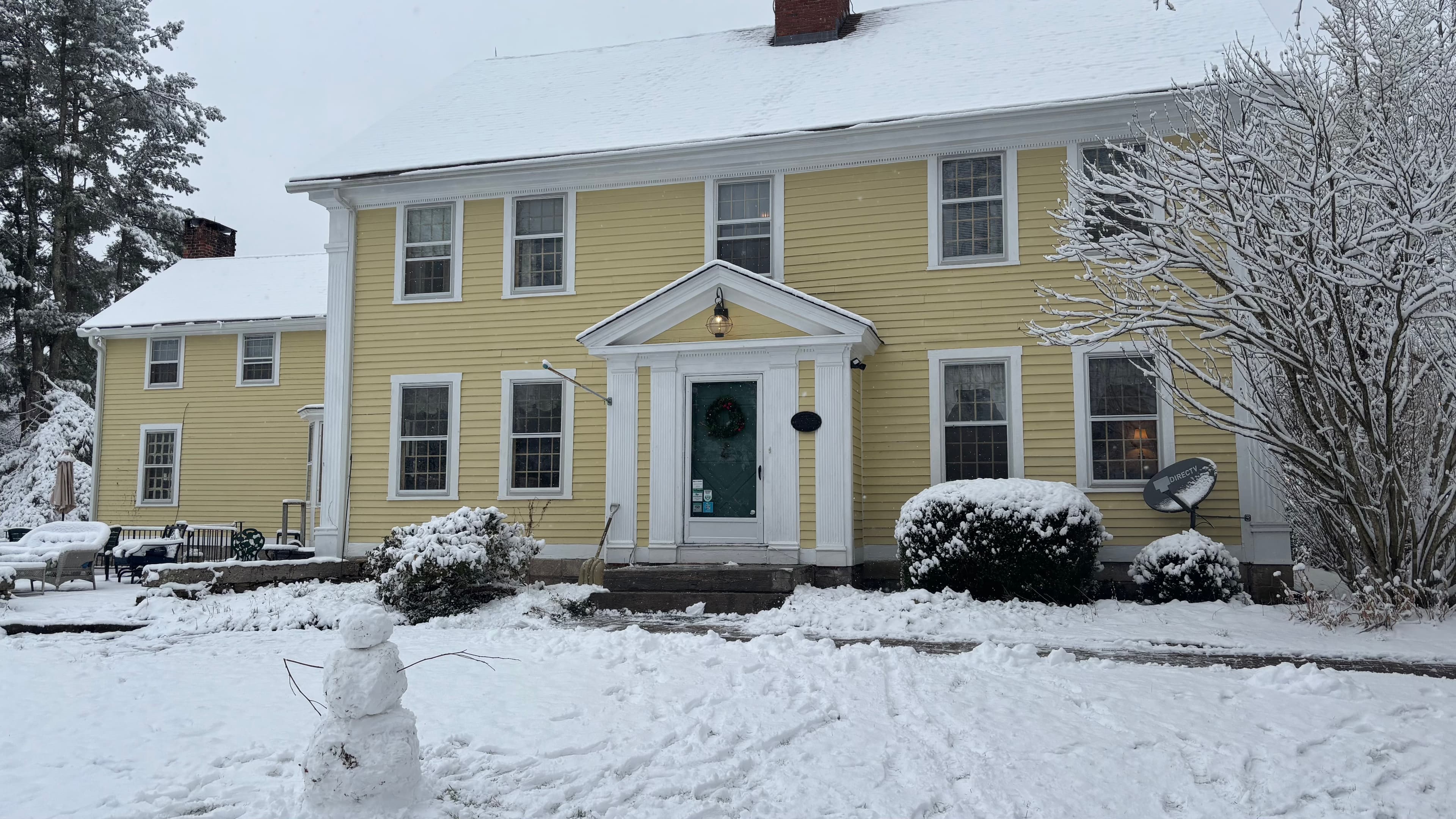 A yellow house with snow-covered grounds and a small snowman in the front yard.