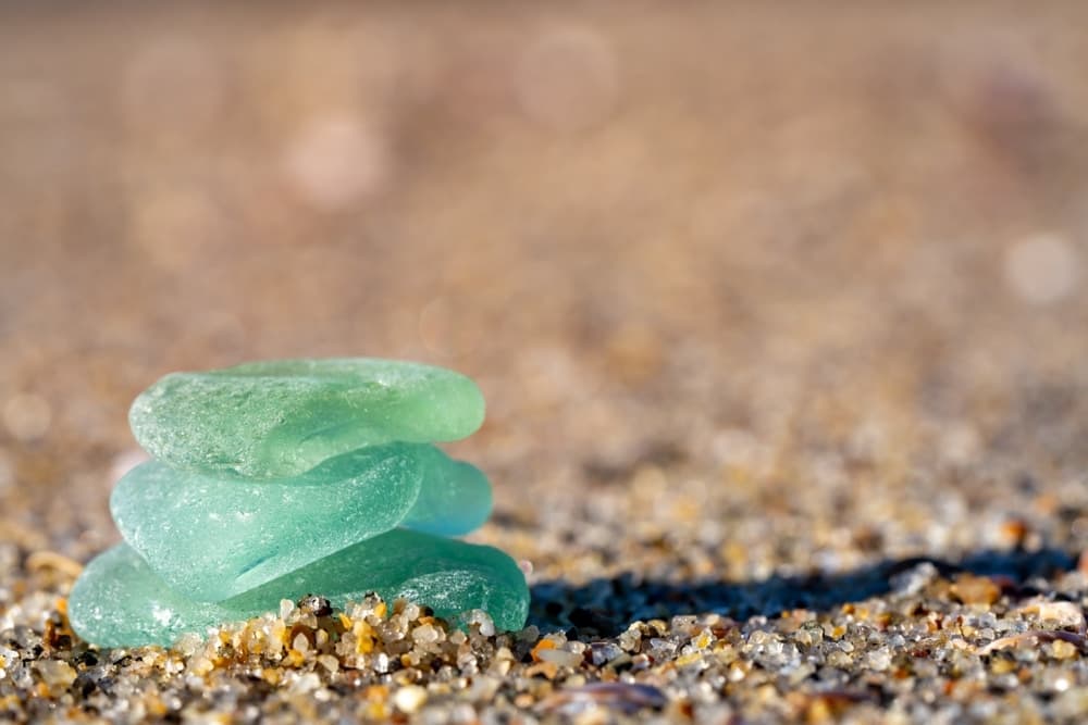 A small stack of smooth, green sea glass on sandy beach.