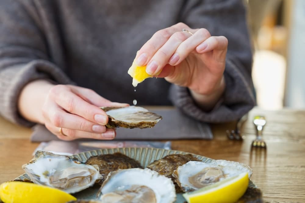 A person squeezes lemon juice onto an oyster sitting on a decorative plate.