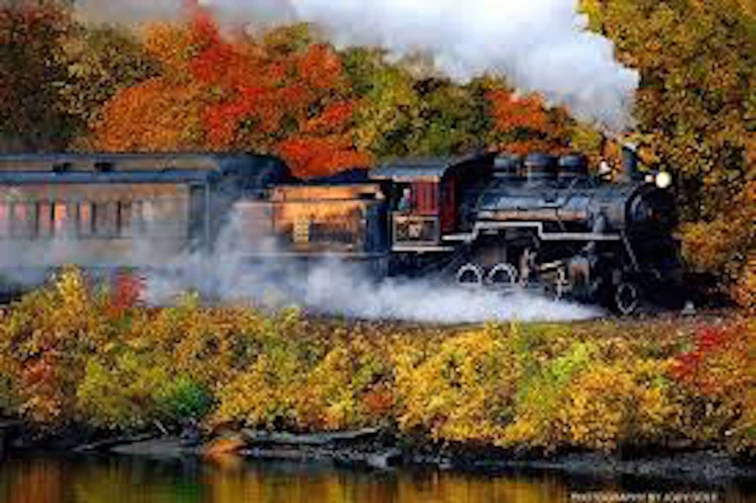 A steam locomotive travels through vibrant autumn foliage.