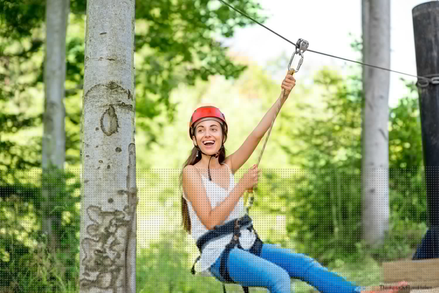 Young woman in a red helmet joyfully zip-lining through a forested area. Young woman in a red helmet joyfully zip-lining through a forested area.