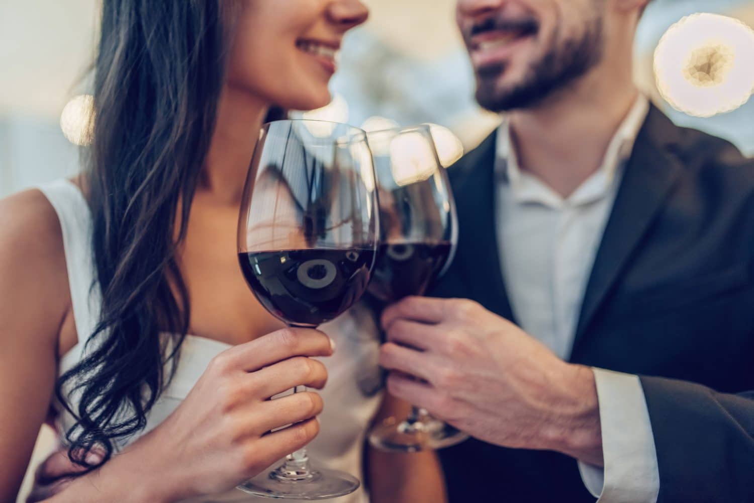 A couple toasts with glasses of red wine, smiling at each other in an elegant setting.