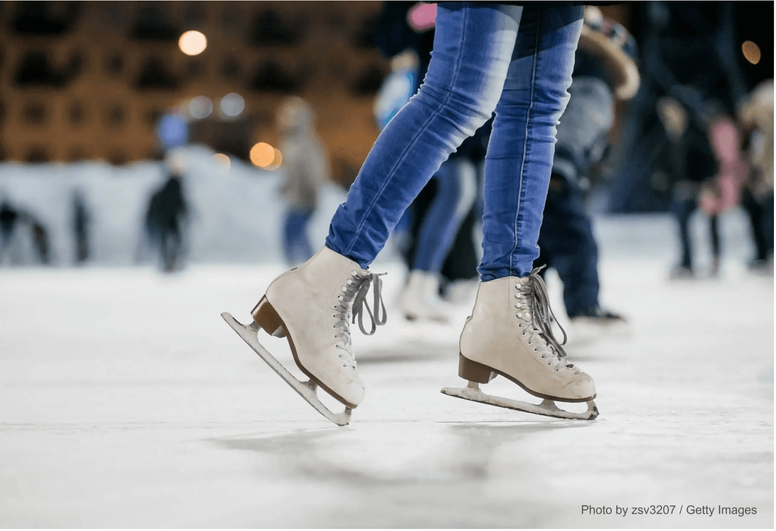 A pair of ice skates gliding on a rink with blurred figures in the background.