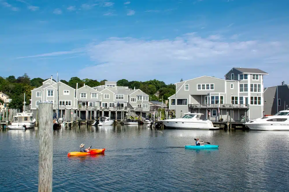 The best things to do in Mystic, CT. Two people enjoying the Mystic River via kayak with buildings in the background